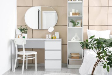 Yatak odasındaki bej fayans duvarının yanında makyaj masası ve kozmetik ürünler.