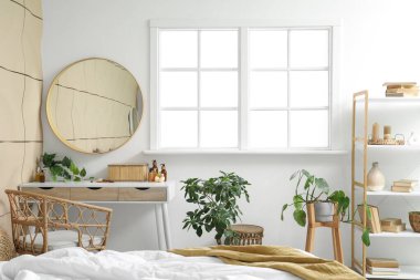 Yatak odasının penceresinin yanında makyaj masası kozmetik ürünleri ve ev bitkisi.