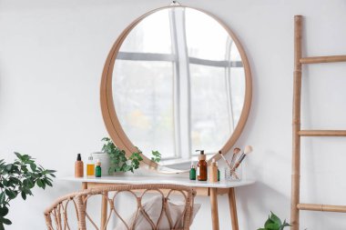 Yatak odasındaki beyaz duvarın yanında makyaj masası kozmetik ürünler ve ayna.