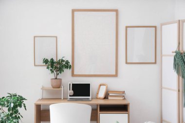 Beyaz duvarda dizüstü bilgisayarı ve boş posterleri olan işyeri.