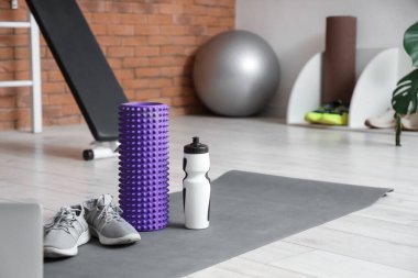 Spor ayakkabılı köpük silindir ve spor salonundaki minderde su şişesi.