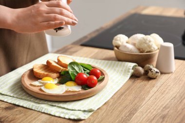 Kadın, mutfakta kızarmış bıldırcın yumurtaları, taze sebzeler ve tostlarla lezzetli bir akşam yemeği hazırlıyor.