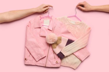 Pembe arka planda şık, sıcak çocuk kıyafetleri olan kadın elleri.