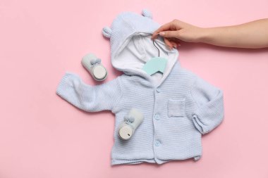 Şık bebek süveteri ve pembe arka planda çorapları olan bir kadın eli.