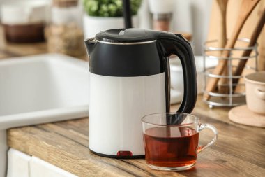 Modern elektrikli su ısıtıcısı ve bir bardak sıcak çay mutfakta tezgahta.