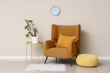 Koltuk, puf. Beyaz duvardaki çiçek ve saat.