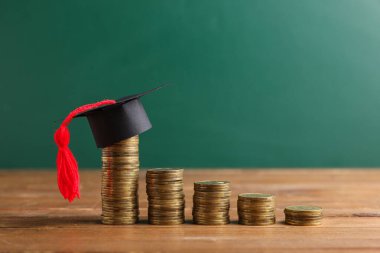 Mezuniyet şapkalı bozuk paralar yeşil karatahtanın yanındaki masada, yakın plan. Öğrenci kredisi kavramı
