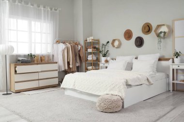 Konforlu yatak, çekmeceler ve modern yatak odasındaki giysili askılar.