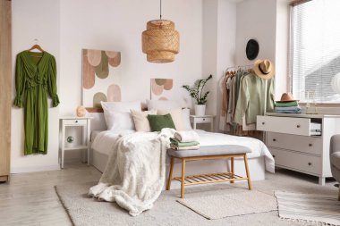 Rahat bir yatak, çekmeceler ve yatak odasının içinde şık kıyafetler.