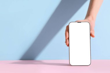 Mavi duvarın yanındaki pembe masada modern cep telefonu olan bir kadın.