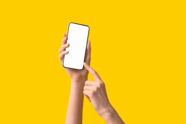 Sarı arka planda modern cep telefonunu tutan kadın eller, yakın plan.