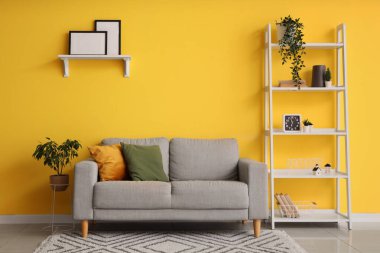 Konforlu kanepe, raf ünitesi ve odanın sarı duvarında boş fotoğraf çerçeveleri.