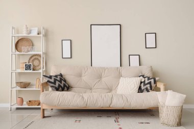 Konforlu kanepe, raf ünitesi ve odadaki bej duvarda boş fotoğraf çerçeveleri.