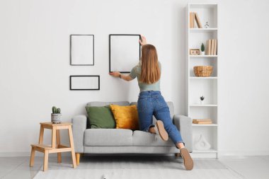 Evdeki beyaz duvara boş fotoğraf çerçevesi asan bir kadın. Arka plan