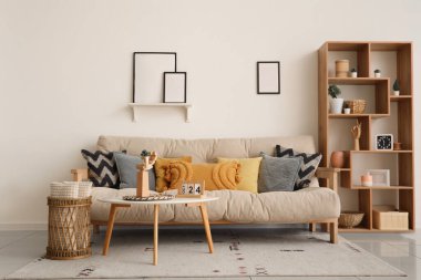 Rahat bir kanepe, kahve masası ve oturma odasındaki beyaz duvarda boş fotoğraf çerçeveleri.