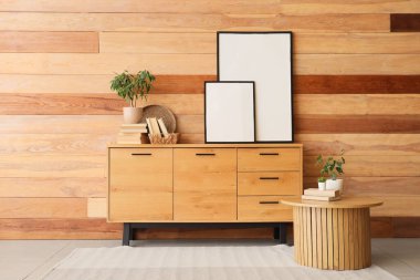 Oda odasındaki ahşap duvarın yanında boş fotoğraf çerçeveleri olan sehpa ve çekmeceler.