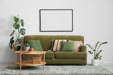 Rahat bir kanepe, kahve masası ve beyaz duvarda boş bir fotoğraf çerçevesi.