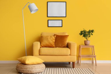 Koltuk ve boş fotoğraf çerçeveleri sarı duvarda.