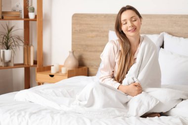 Genç bir kadının yatakta oturduğu bir sabah.