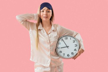 Pembe arka planda pijamalı ve uyku maskeli genç bir kadın.