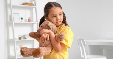 Little Asian girl with autistic disorder hugging toy bear at home clipart