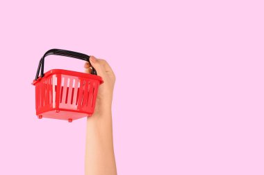 Pembe arka planda mini alışveriş sepeti tutan kadın.