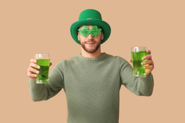 Kahverengi arka planda bira bardakları olan cüce şapkalı genç bir adam. Aziz Patrick Günü kutlaması