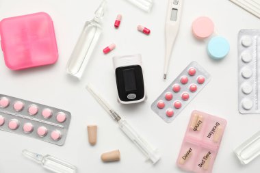 Nabız oksimetresi, termometre, kontak lensli konteynır ve beyaz arka planda ilaç bileşimi