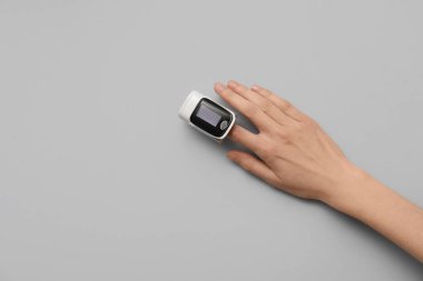 Gri arkaplanda nabız oksimetresi olan bir kadın el.