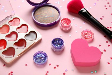 Parıltı kavanozları, konfeti, makyaj ürünleri ve pembe arka planda fırça içeren kompozisyon, yakın plan.