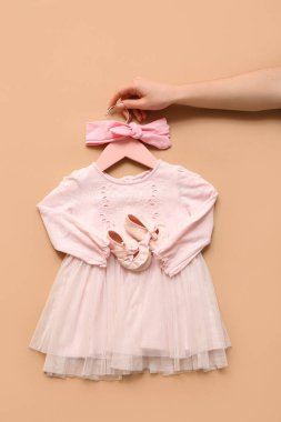 Şık bir bebek elbisesi, patik ve saç bandı olan kadın eli.