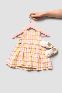 Şık bir bebek elbisesi ve gri arka planda kalçaları olan kadın eli.