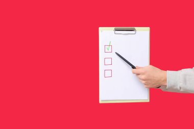 Kırmızı arka planda boş liste kutusu tutan bir adam var. Anket konsepti