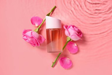 Güzel pembe gülleri olan bir şişe parfüm ve renkli arka planda su yaprakları.
