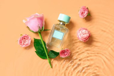 Bir şişe parfüm ve sarı arka planda suda güzel pembe güller.
