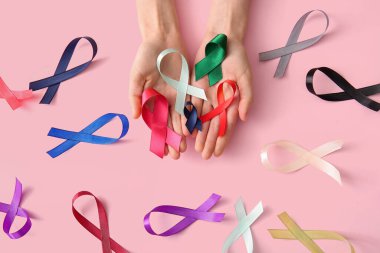 Pembe arka planda farklı kurdeleleri olan kadın eller, yakın plan. Dünya Kanser Günü