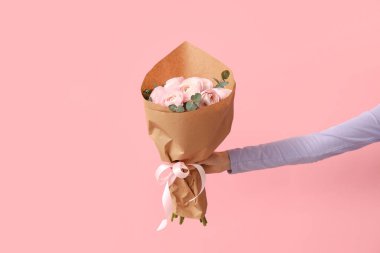 Pembe arka planda bir buket ranunculus çiçeğiyle kadın eli.