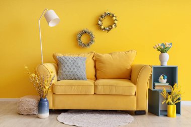 Sarı kanepe, lamba ve Paskalya çelenkleri olan oturma odasının içinde.