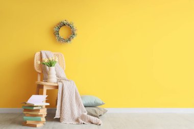 Laleli sandalye, kitaplar ve sarı duvarda Paskalya çelengi.