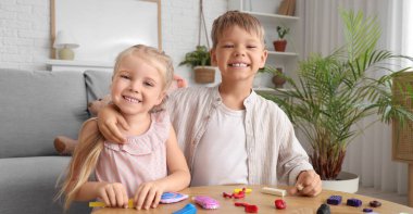 Evdeki masada plastikten heykel yapan sevimli çocuklar.