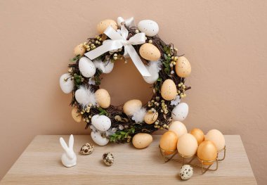 Bej duvarın yanındaki masada yumurtalı Paskalya çelengi.