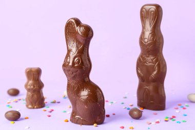 Çikolatalı Paskalya tavşanları ve mor arka planda yumurtalar.