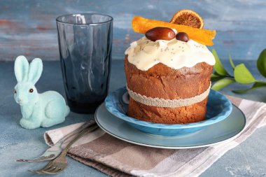 Mavi grunge duvarının yanındaki masada tavşan figürlü ve camlı Paskalya pastası.