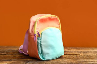 Turuncu duvarın yanındaki ahşap masada renkli okul çantası.