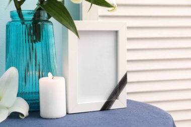 Boş cenaze çerçevesi, yanan mum ve vazo, masada zambak çiçekleri, yakın plan.