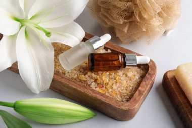 Ahşap tahta, deniz tuzu, gerekli yağ şişeleri ve gri arka planda zambak çiçekleri, yakın plan.