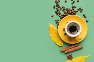 Yeşil arka planda bir fincan aromatik kahve, fasulye ve sonbahar yapraklı kompozisyon