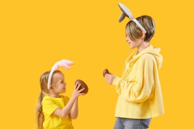 Sarı arka planda çikolatalı yumurtaları olan tavşan kulaklı şirin çocuklar. Paskalya kutlaması