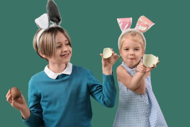 Yeşil arka planda çikolatalı yumurtaları olan tavşan kulaklı şirin çocuklar. Paskalya kutlaması