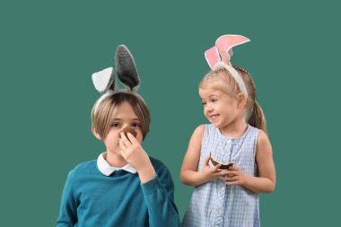 Yeşil arka planda çikolata yumurtası olan tavşan kulaklı şirin çocuklar. Paskalya kutlaması